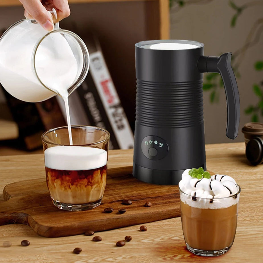 Person pouring milk into a glass of coffee with a milk frother on a wooden table.